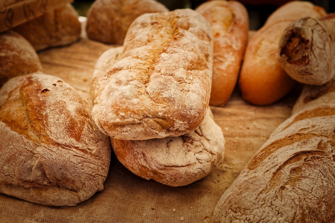 Freshly baked artisan bread loaves displayed at a local market during the afternoon, tantalizing the senses with warm aroma - A variety of artisan bread loaves sit on a rustic cloth at a market, exuding a warm aroma. Their crusty exteriors invite passersby to indulge in this fresh, baked goodness.