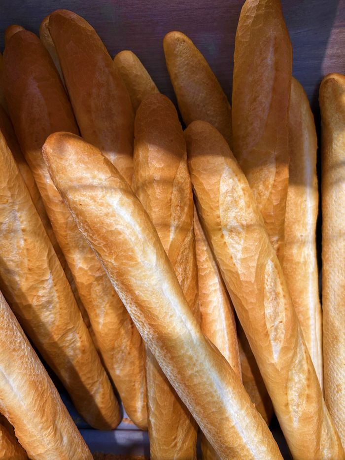 Close-up of freshly baked golden baguettes stacked in a bakery for sale.
