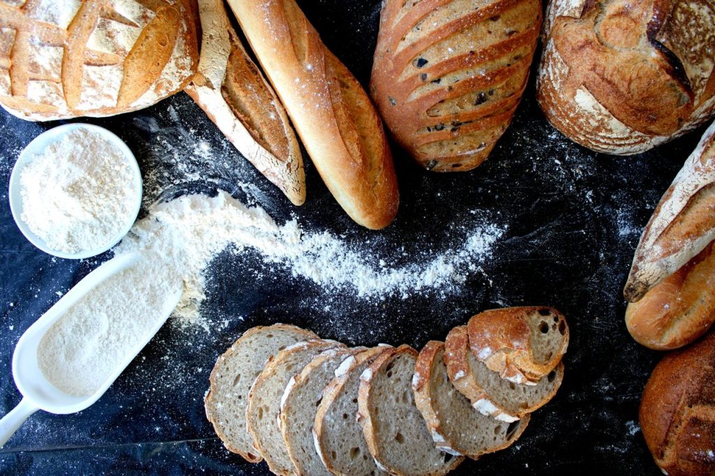 Top view of various freshly baked artisan breads and flour on a dark surface, showcasing texture.