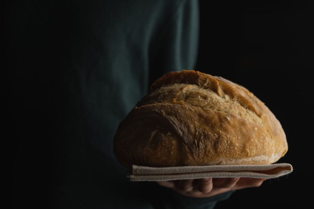 Close-up of a fresh baked loaf of bread held in hands with a dark background.